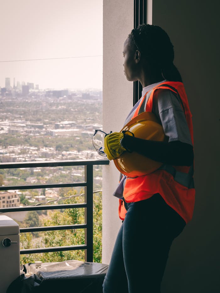 Female engineer in safety vest overlooking the city, holding helmet.